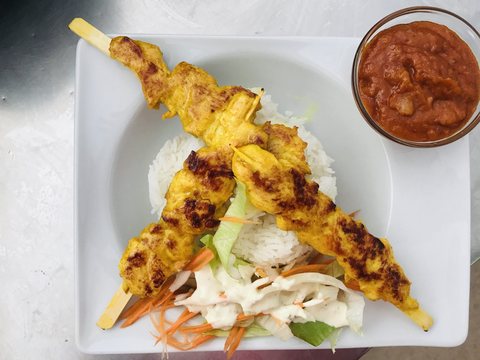 Satay Gai: zwei Hühnerspieße auf Reis und Salat, daneben ein Schälchen Erdnusssauce, auf einem weißen Teller